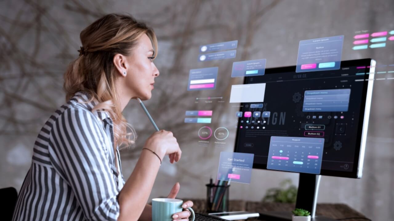 Woman working on digital interface design at a desktop computer with UI/UX elements on screen