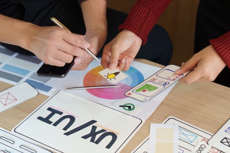 Children using colored pencils to complete alphabet and shape learning worksheets at a classroom table.